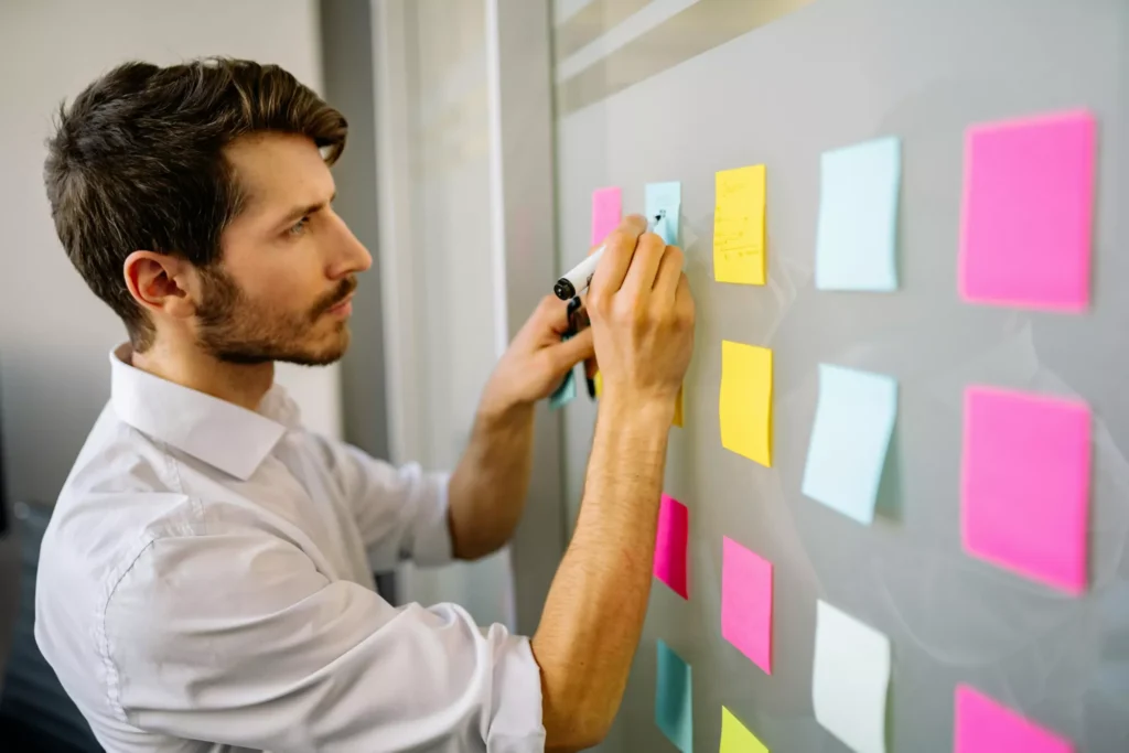 Empresario trabajando frente a una pizarra con post-its, organizando ideas para un estudio de mercado.