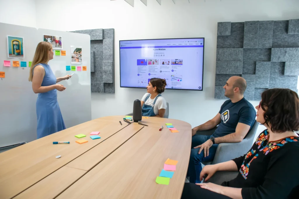 Grupo de personas en una sala de reuniones analizando ideas en una pizarra y una pantalla para planificar estrategias de marketing